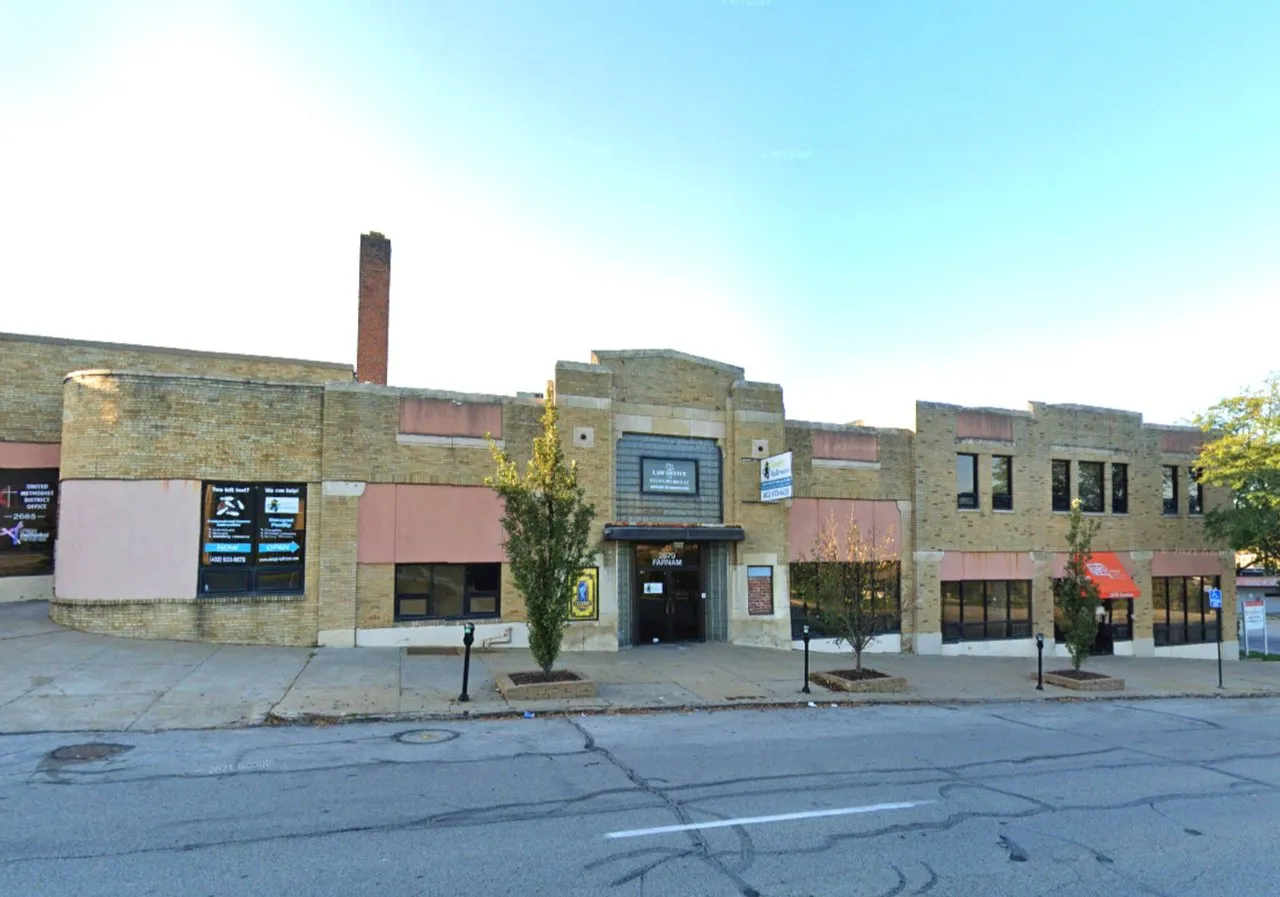 Two-story brick commercial building with storefront windows and a central entrance along a city sidewalk.