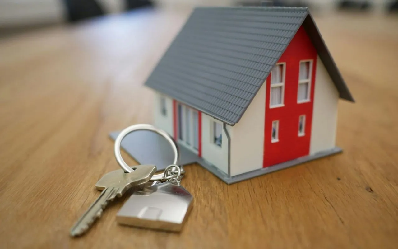 Miniature red-and-white house model beside a set of keys.