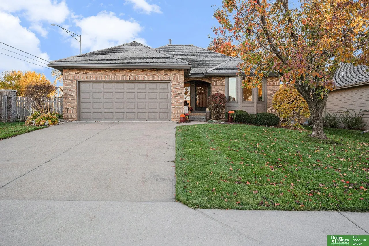 Brick home with a two-car garage, wide driveway, and autumn tree in the front yard.