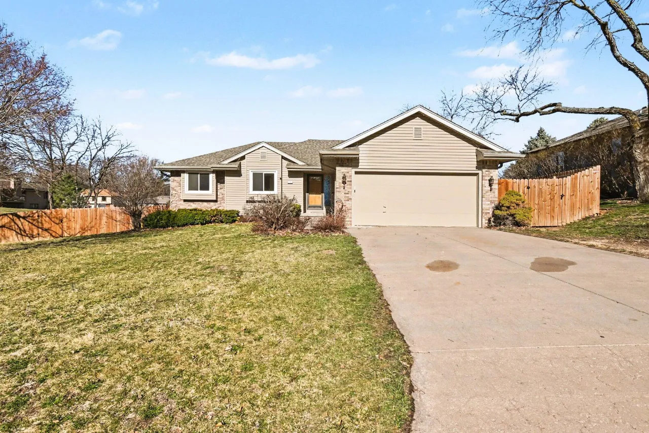 Single-story beige and brick home with a two-car garage, wide driveway, and fenced yard.