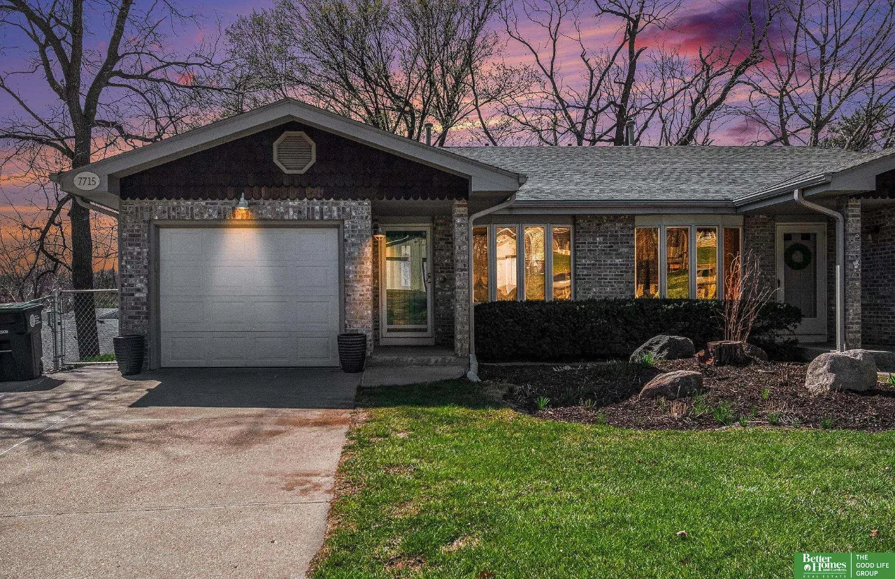 Brick home at dusk with a two-car garage, glowing windows, and a landscaped front yard.
