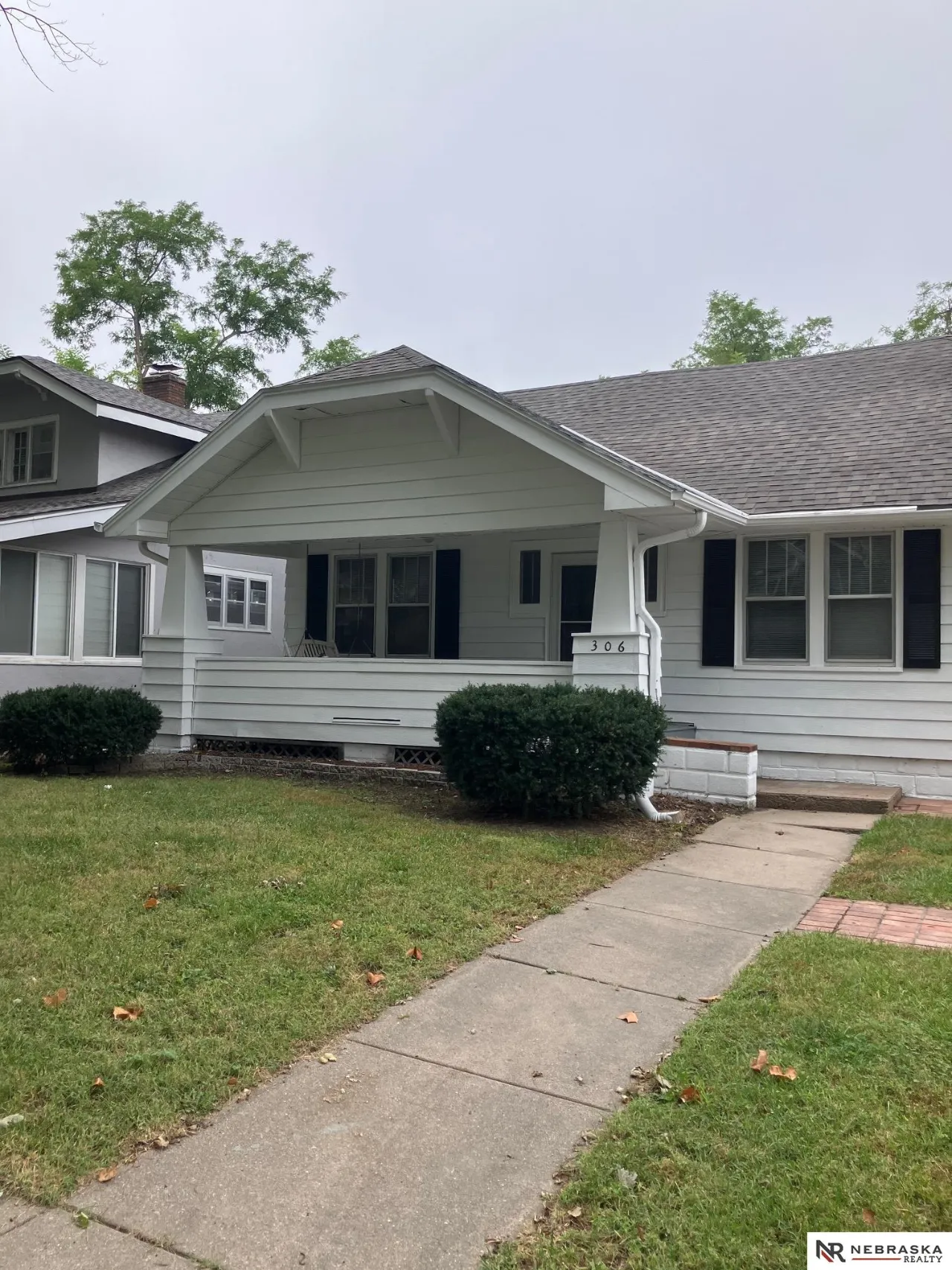 Light gray house with a covered porch, dark shutters, and a walkway leading from the lawn.