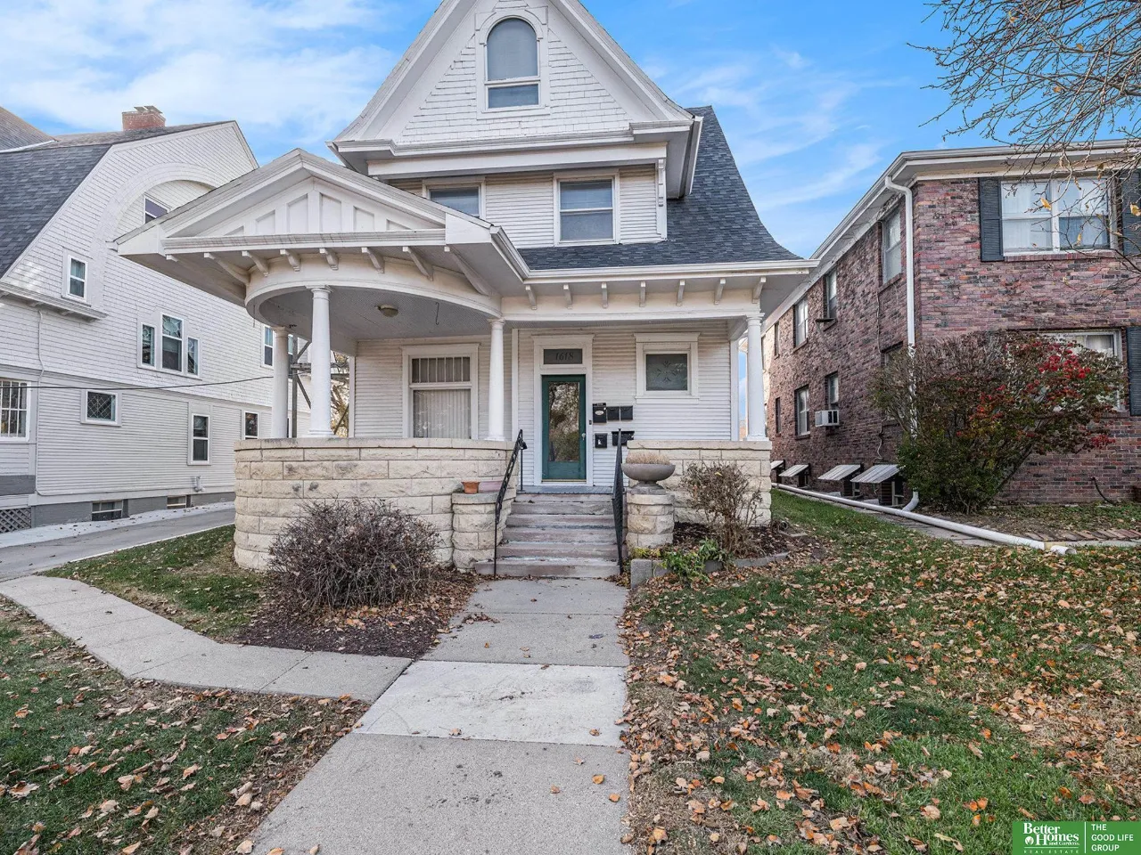 White multi-story house with a covered porch, stone wall, and front steps.