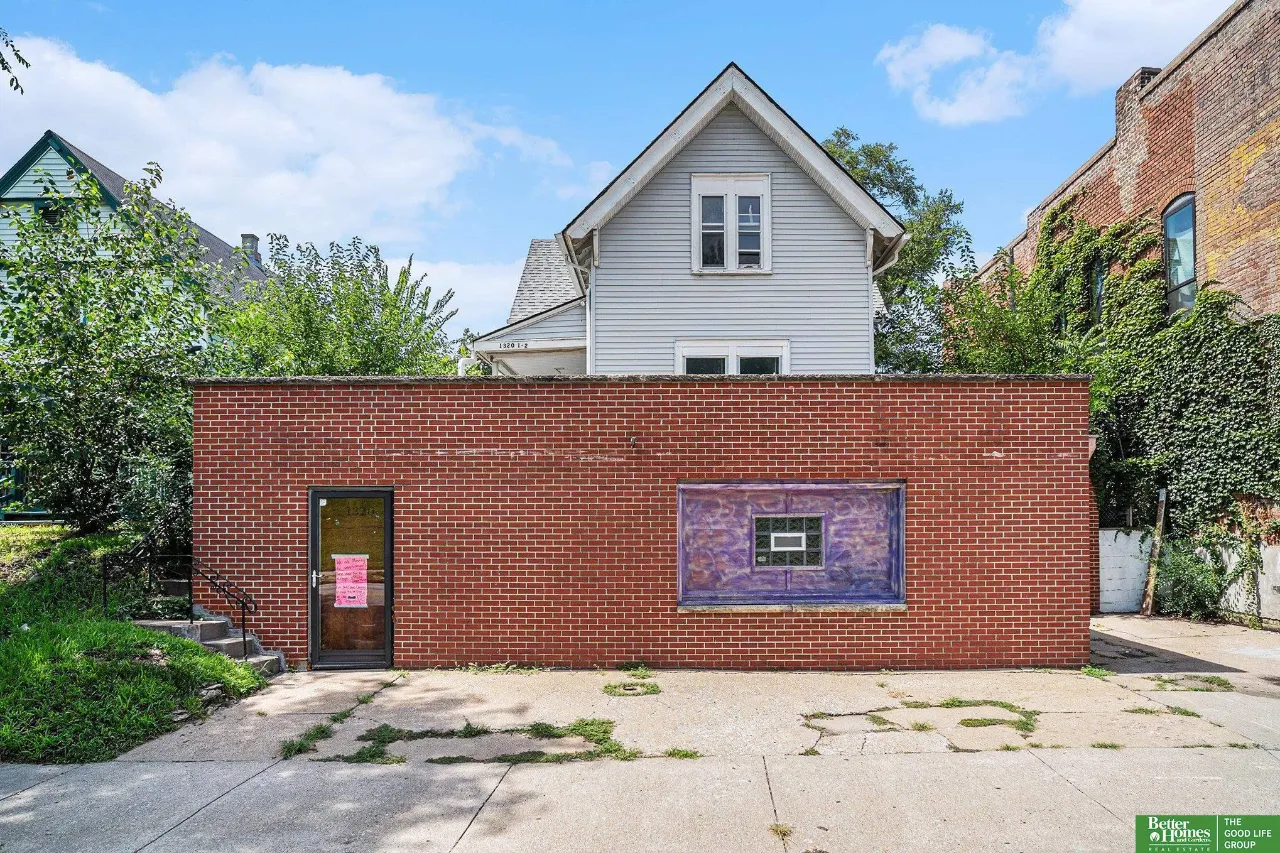 Brick-fronted property with a white gabled house behind it and a purple-framed window.