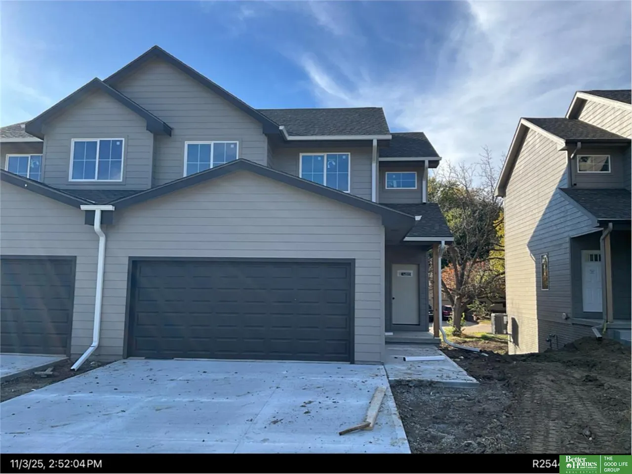 Gray two-story home with dark double garage and a fresh concrete driveway.