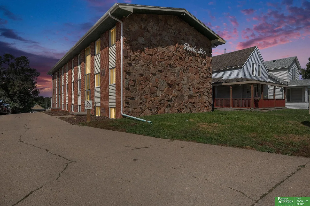 Residential building with a prominent stone facade and Ron Lee sign beside two white houses at dusk.