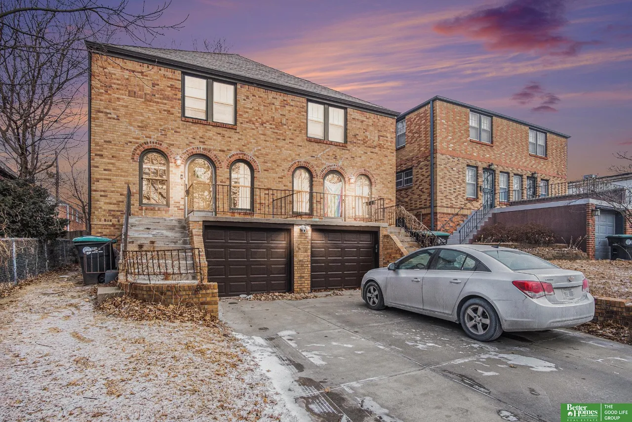 Brick two-story residence with arched windows, twin garage doors, and a silver car in the snowy driveway.