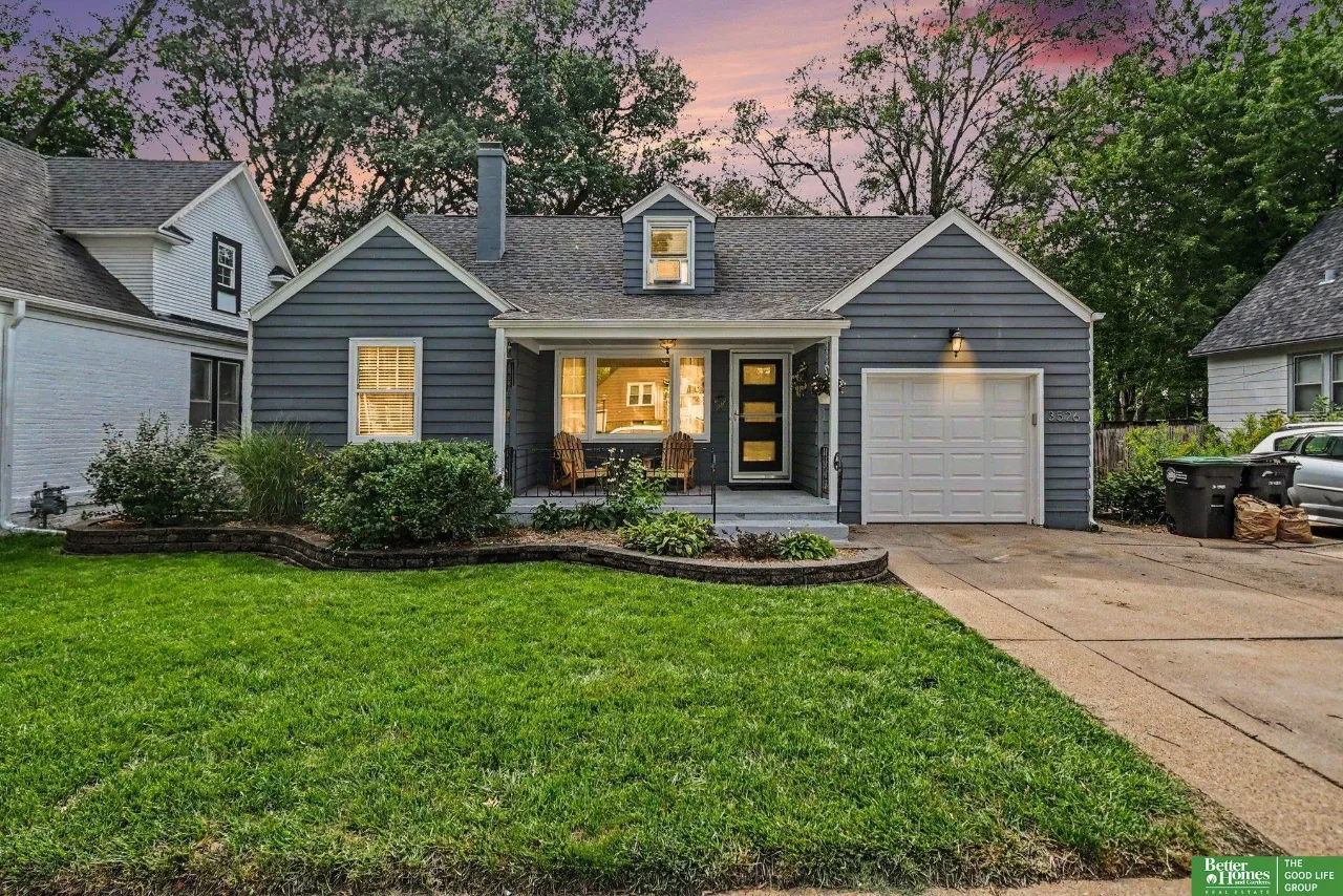 Gray one-story home with a covered porch and attached garage beneath a pink dusk sky.