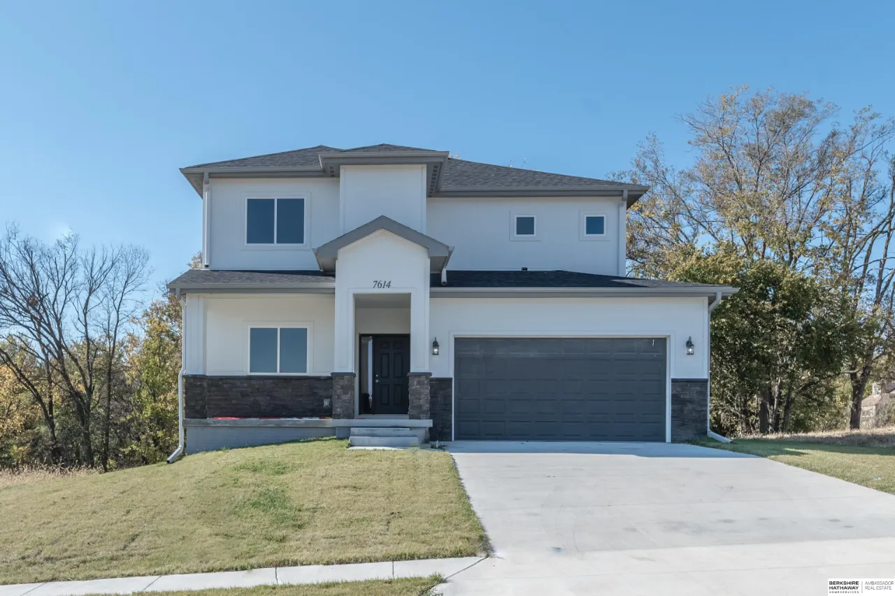 Two-story white house with dark stone accents, covered entry, and attached two-car garage.