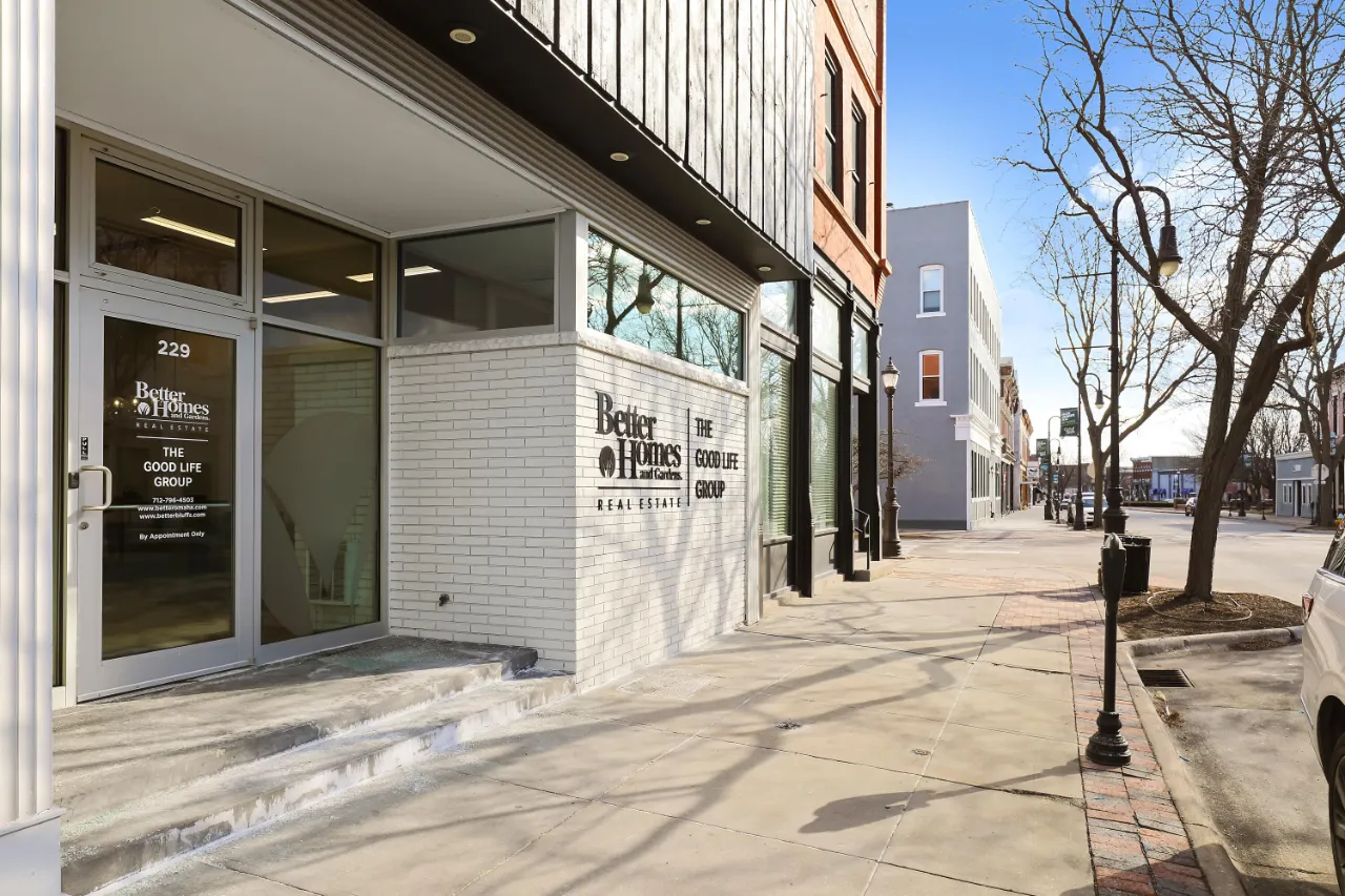 Real estate office storefront with white brick facade and signage on a downtown sidewalk.