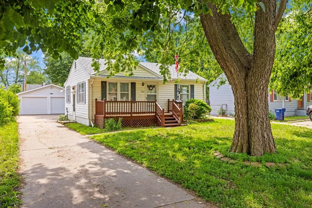 Single-story house with a wooden front porch, detached garage, and large shade tree.