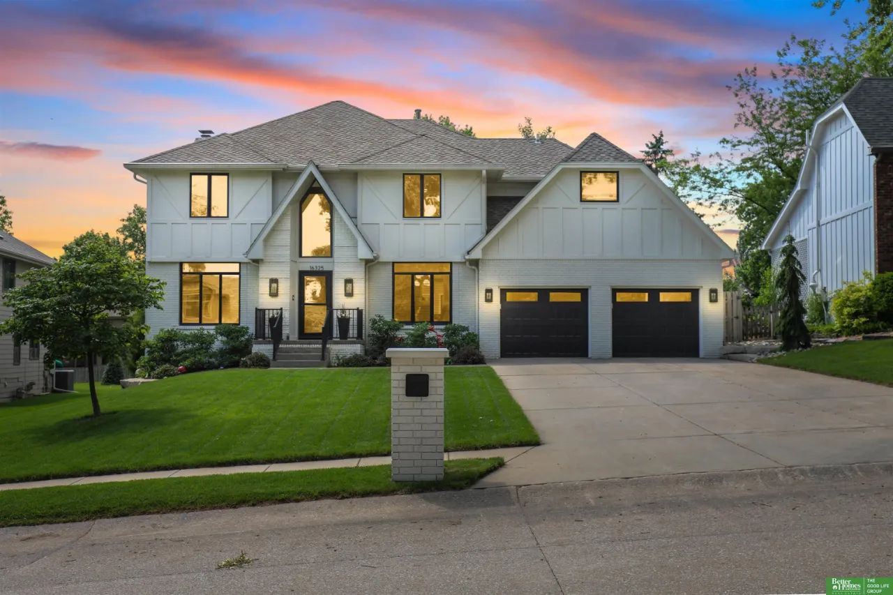White two-story home with twin garage doors and a landscaped lawn at sunset.