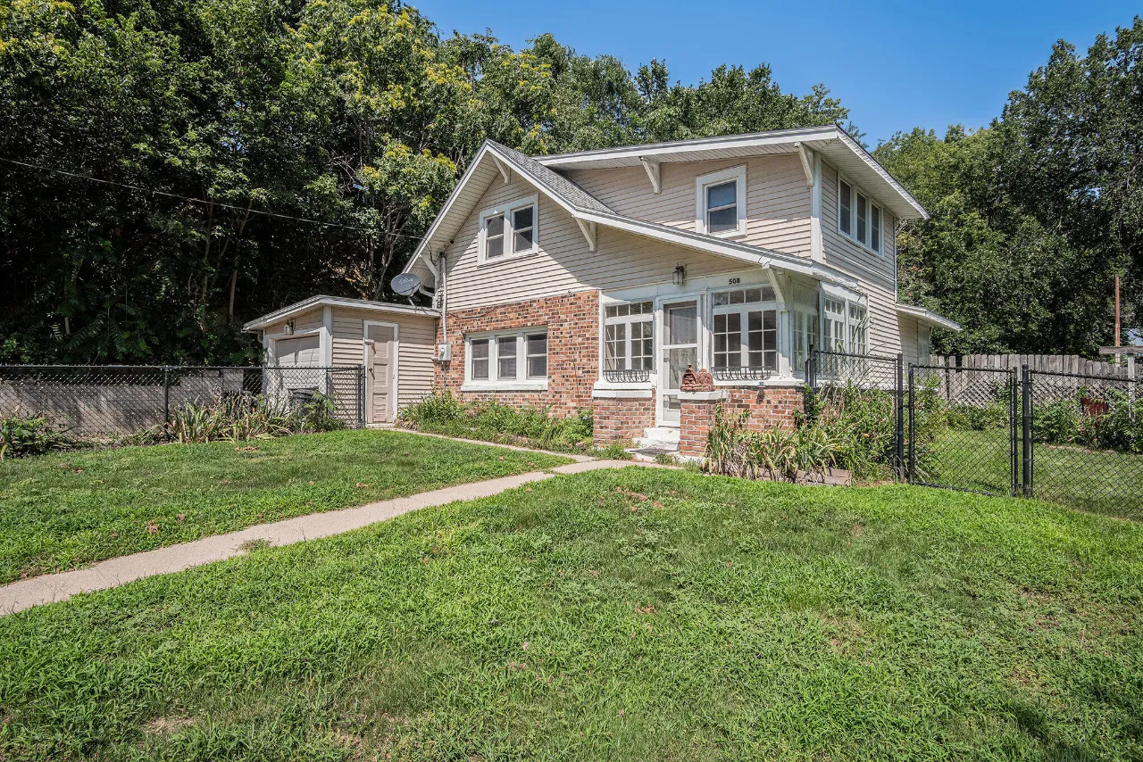Two-story home with a brick facade, enclosed porch, and fenced lawn.