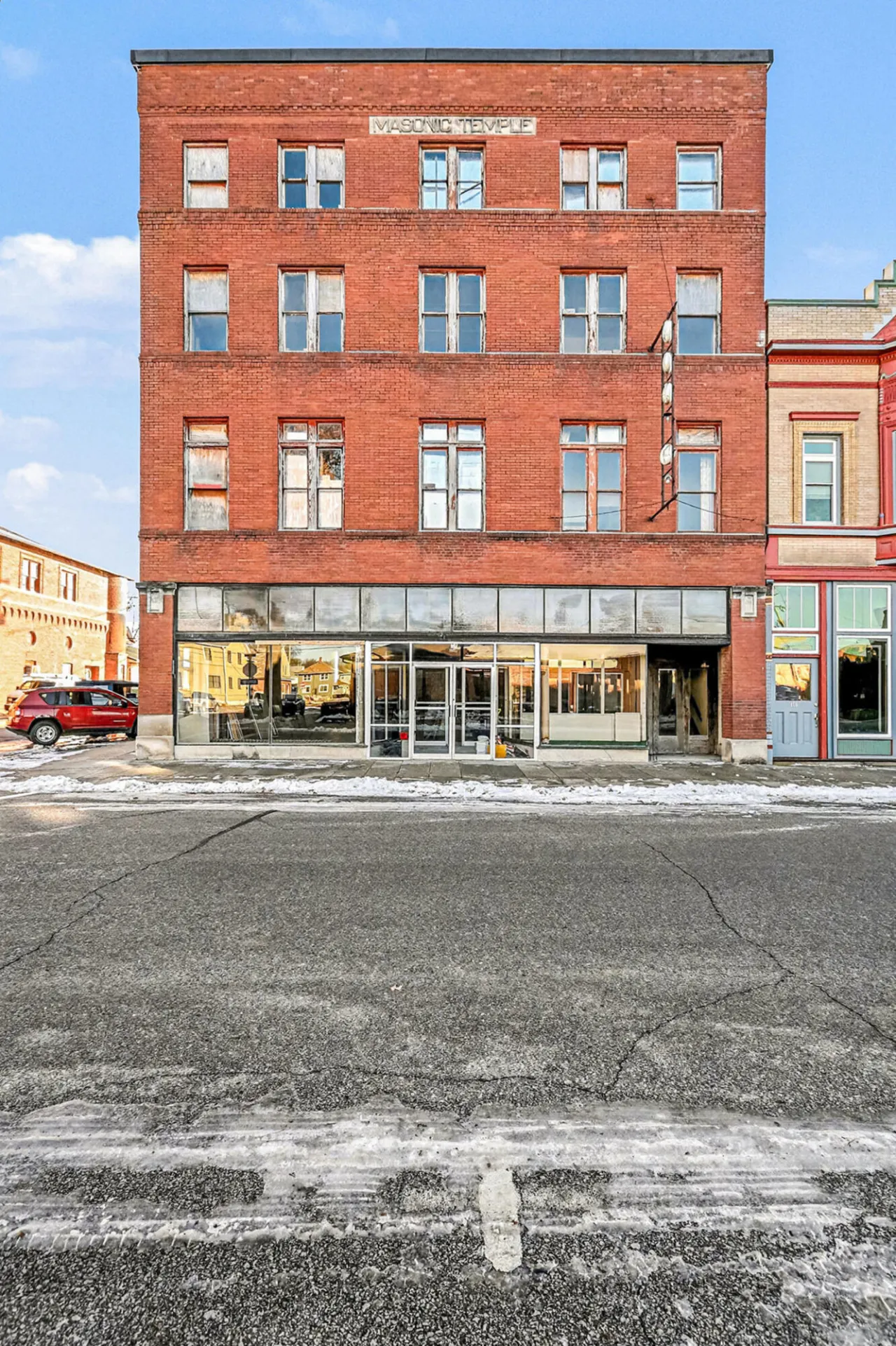 Red-brick Masonic Temple building with storefront windows and snow along the street.