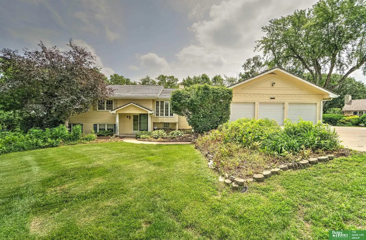 Beige split-level home with a three-car garage, landscaped beds, and a broad green lawn.