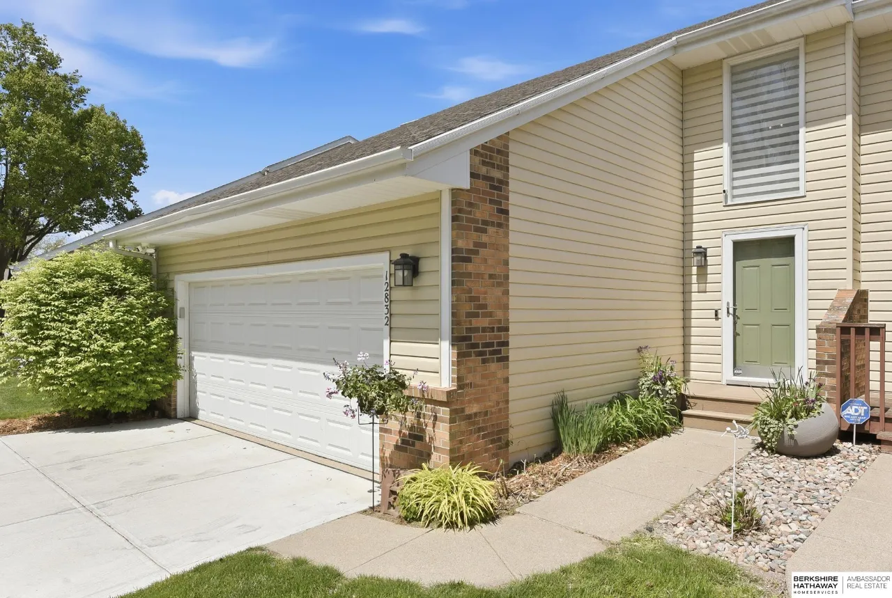 Two-story beige-sided home with brick accents, a double garage, green front door, and landscaped entry.