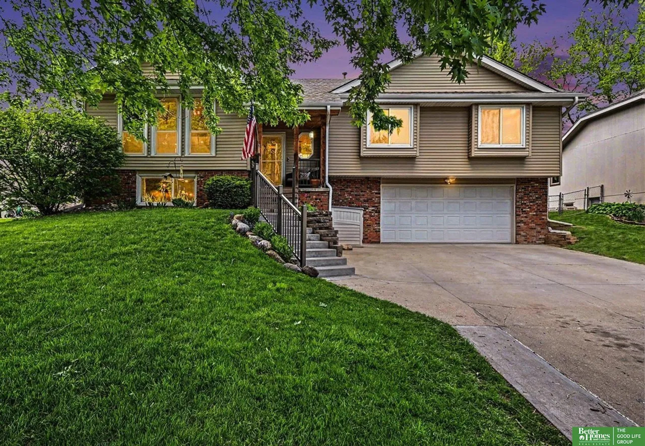 Split-level home with brick and siding, attached garage, flag by the entrance, and a broad lawn.