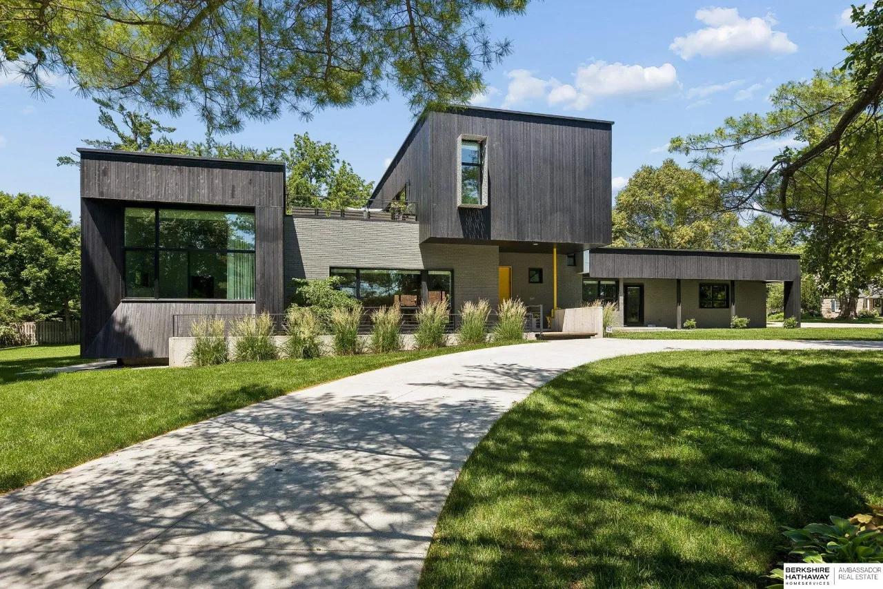 Modern home with dark wood siding, large windows, and a curved concrete driveway.