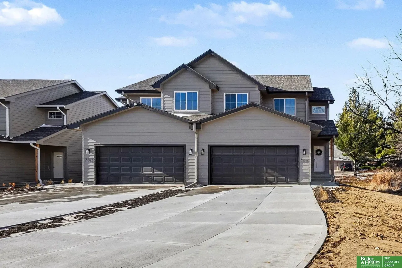 Gray two-story attached home with two dark double garage doors and a wide concrete driveway.