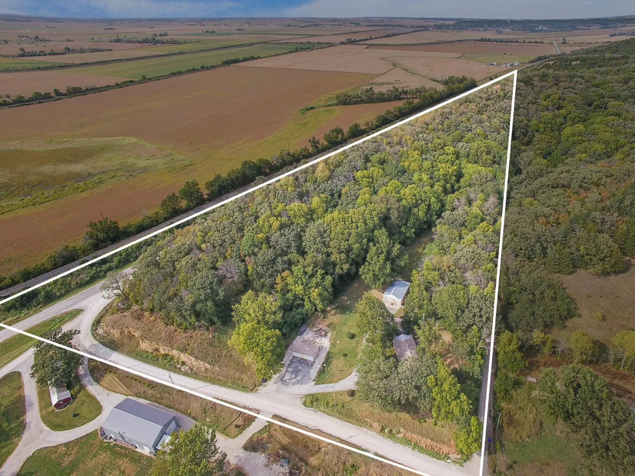Aerial view of a wooded rural property outlined in white, with a road and a few buildings.