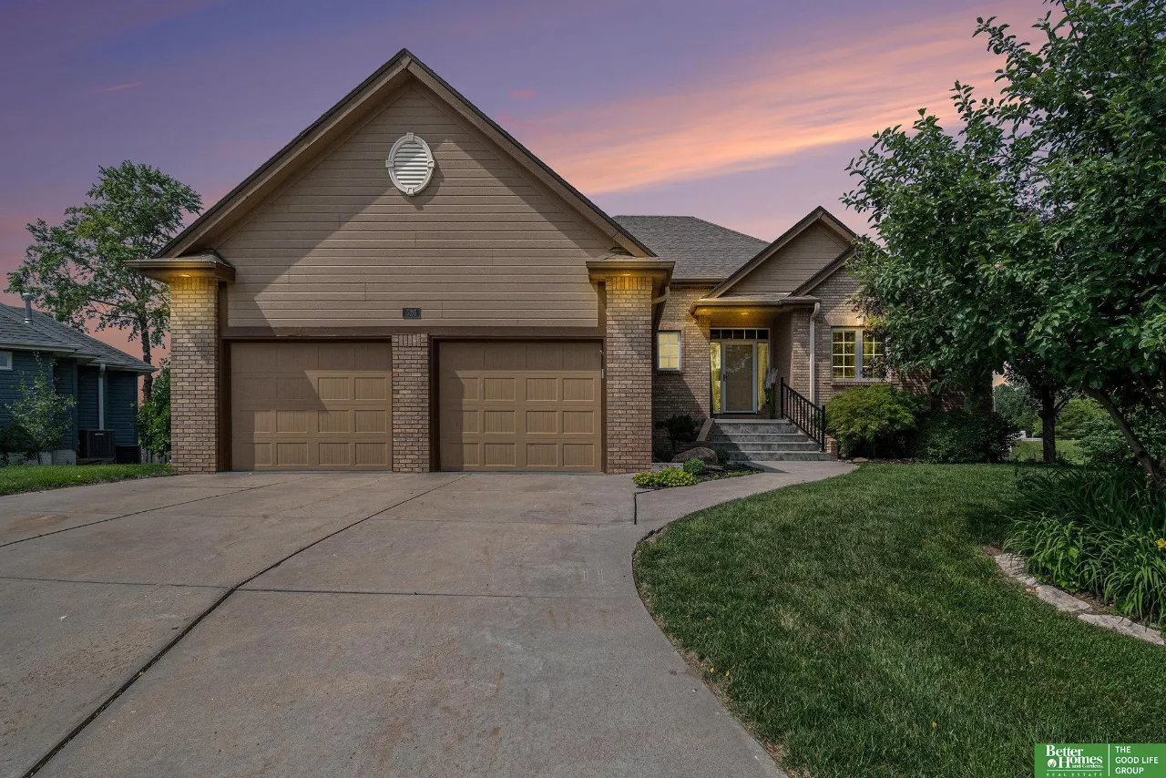 Home at dusk with a two-car garage, brick facade, landscaped lawn, and curved driveway.