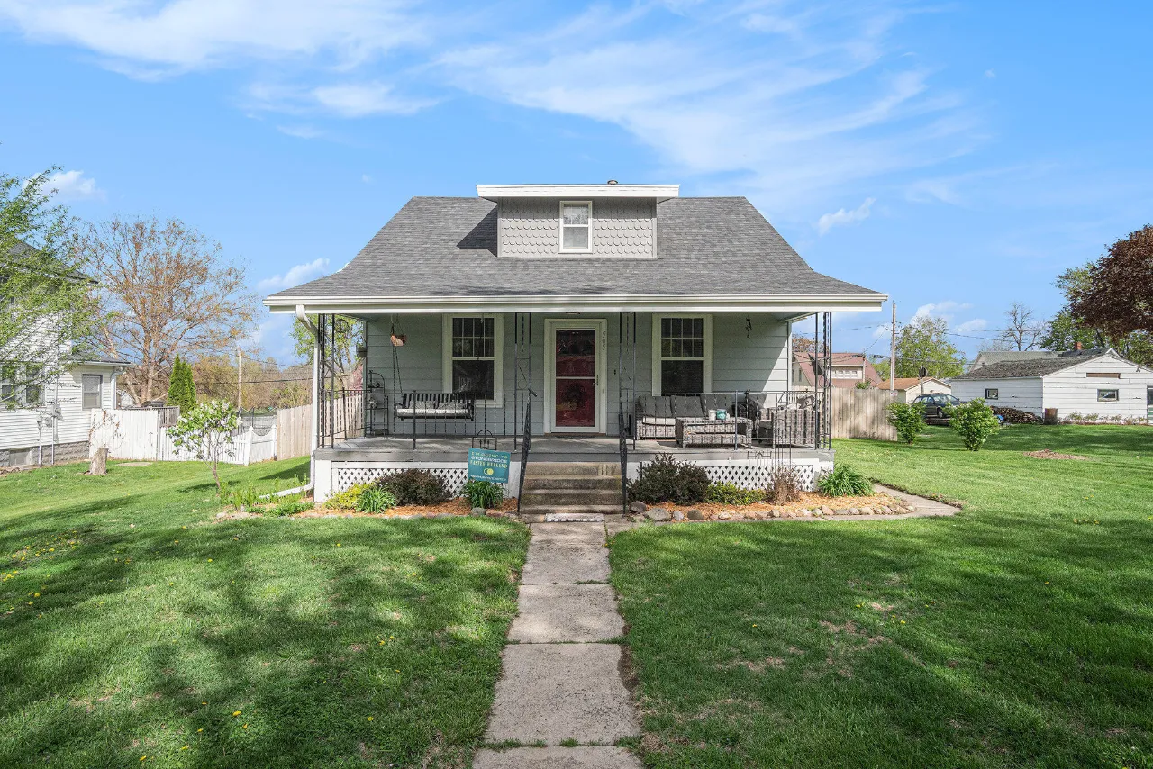 Gray house with a covered front porch, central roof dormer, and walkway through the lawn.