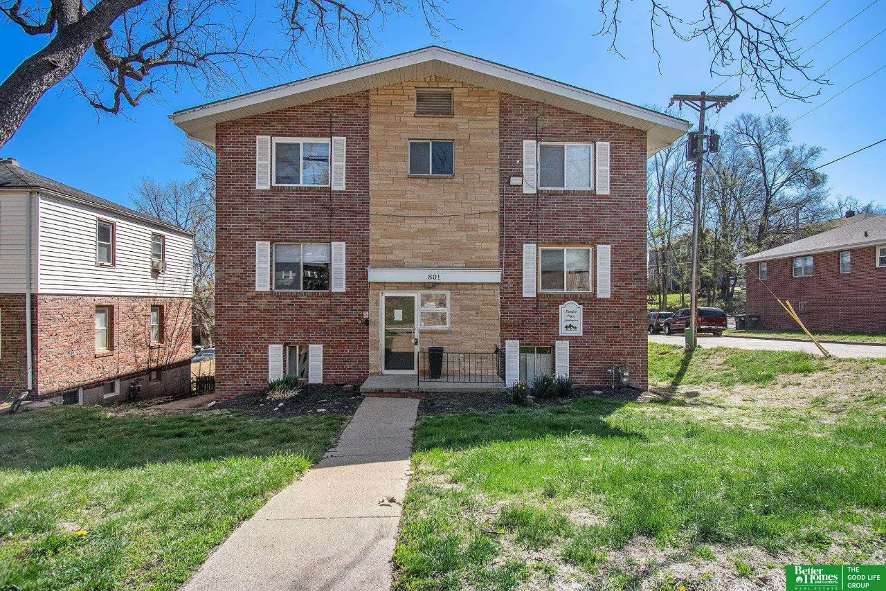 Brick apartment building with a tan stone center, white shutters, and a walkway leading to the entrance.