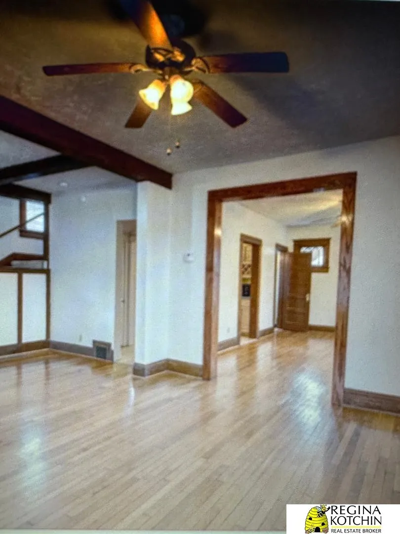 Vacant interior with polished hardwood floors, dark wood trim, and a ceiling fan with lit lamps.