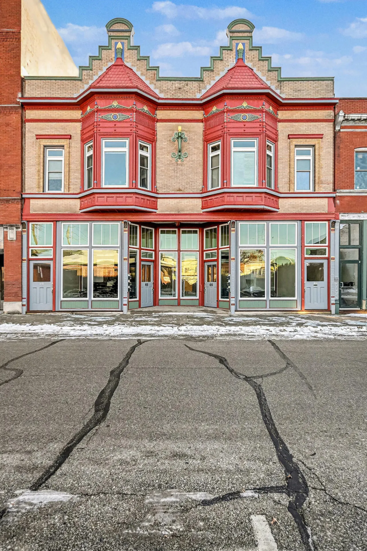 Brick storefront with ornate red bay windows and snow along the sidewalk.