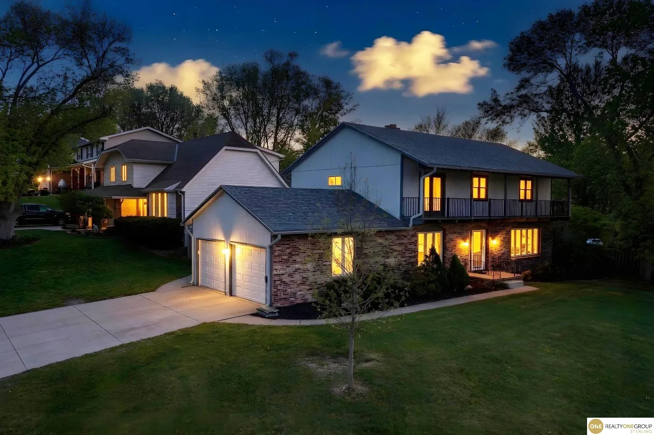 Two-story brick and siding home with a covered balcony and warmly lit windows at night.